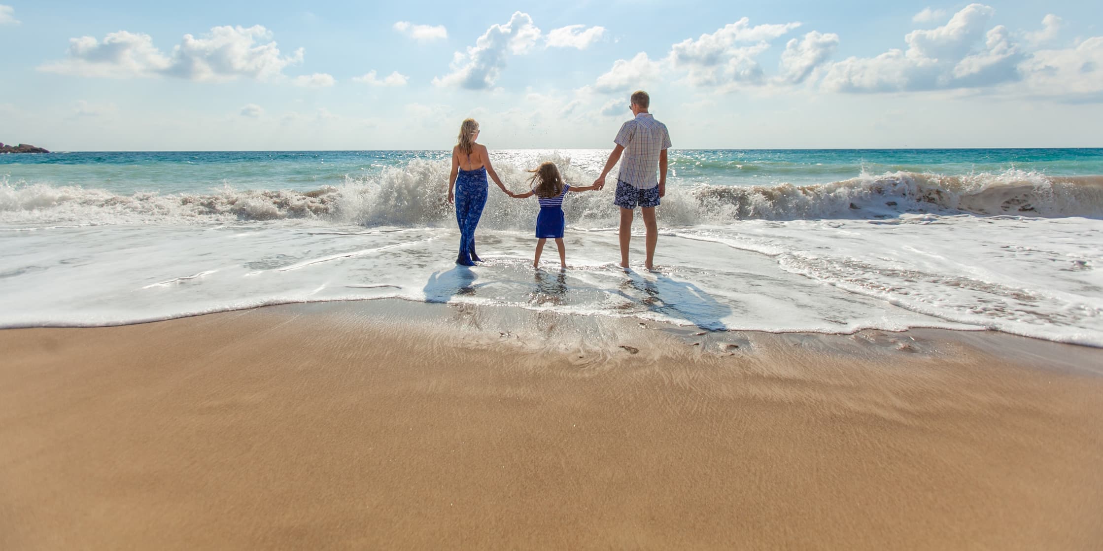 A man, woman, and child holding hands in front of crashing beach waves